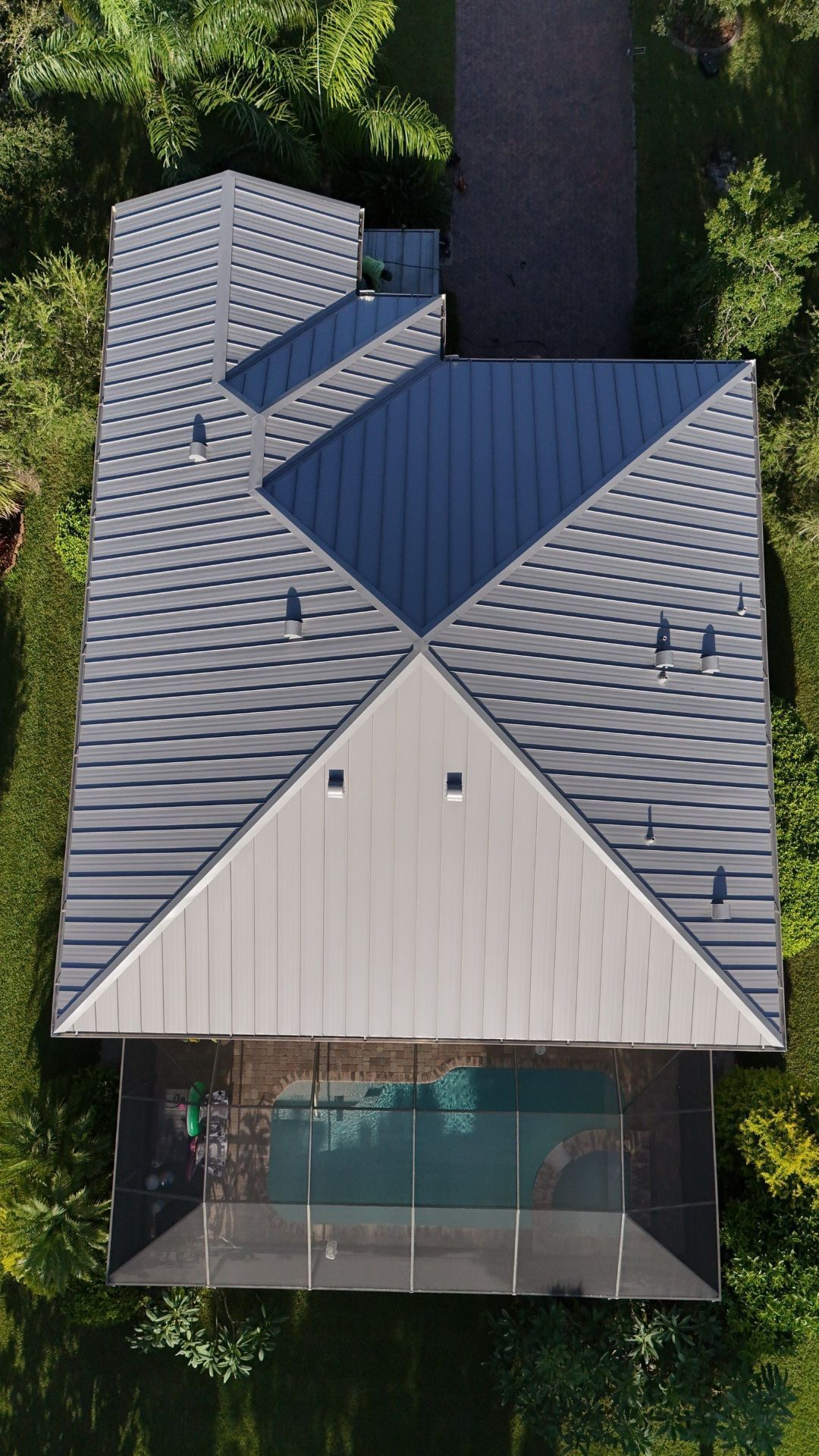 Aerial view of a modern house with a gray and blue geometric roof and a glass-fronted entry.