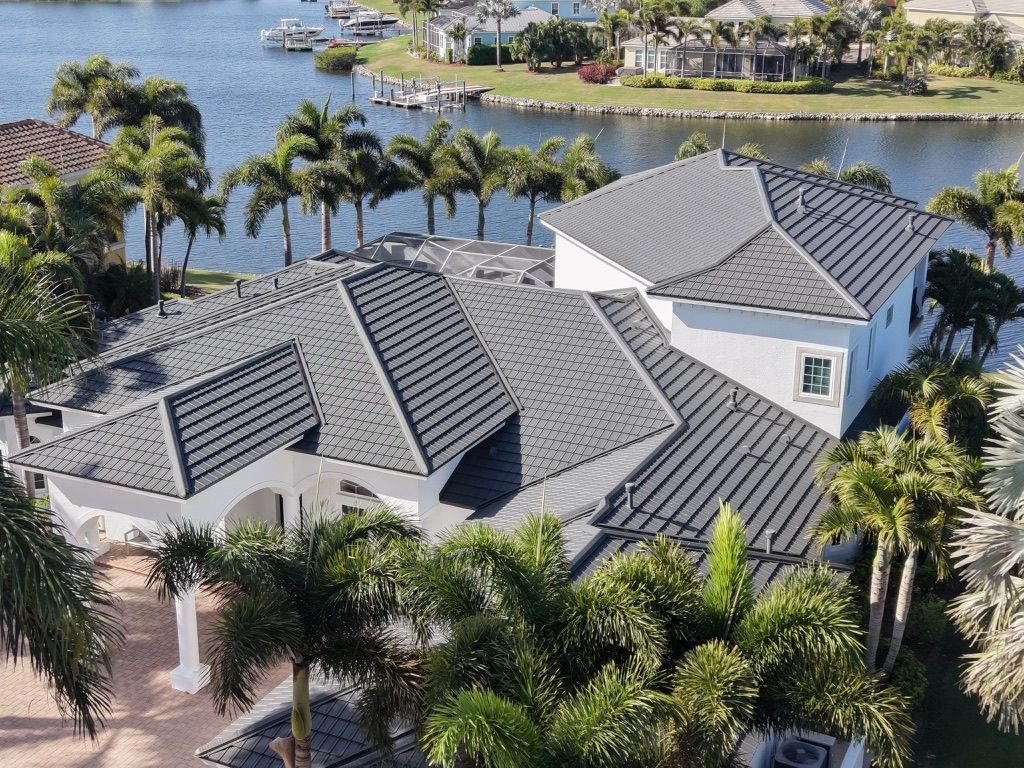 Aerial view of a gray-tiled waterfront house surrounded by palm trees and water.
