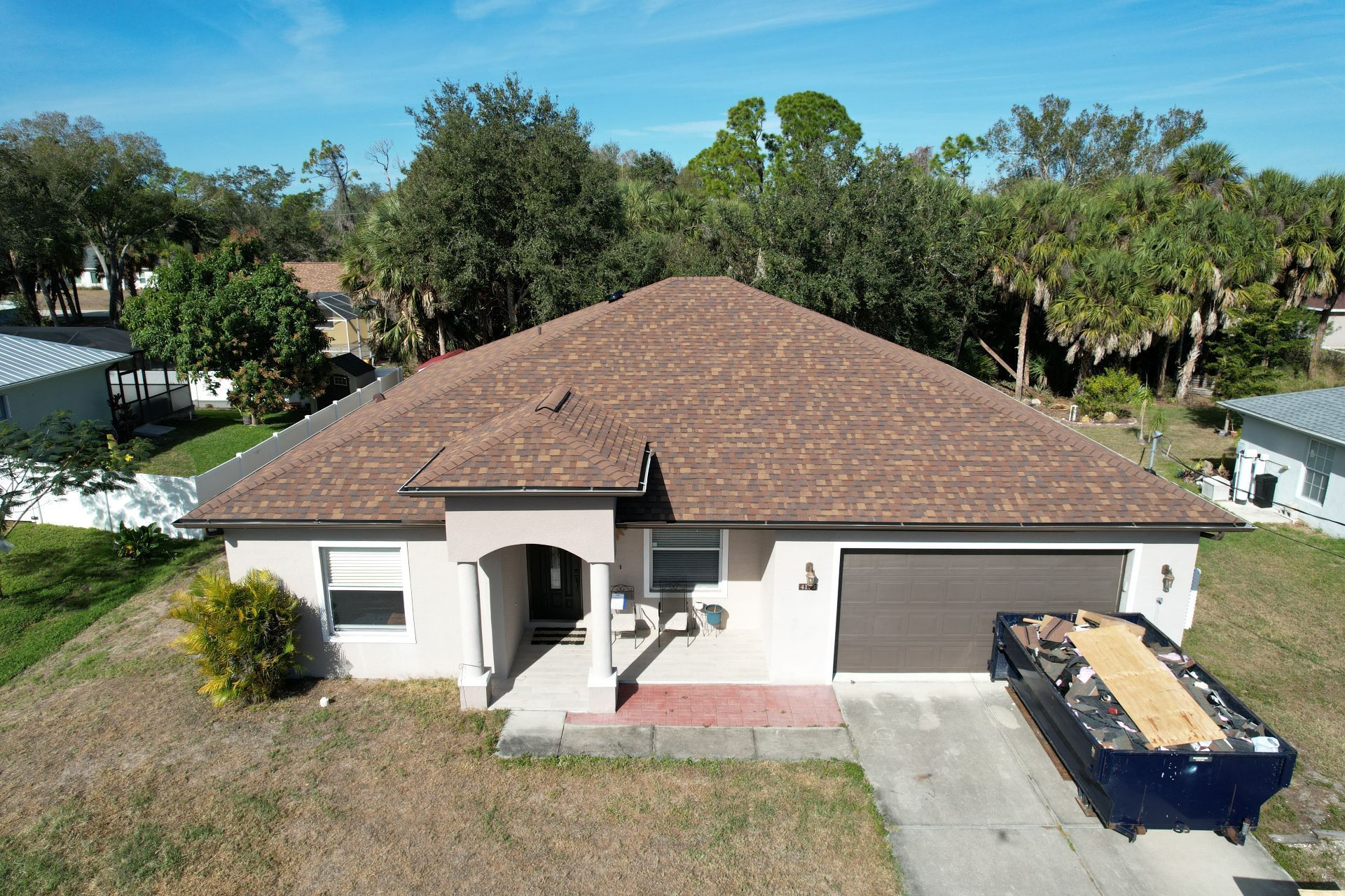 Single-story white house with brown roof and driveway, seen from above, with a dumpster in front