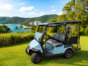 Blue golf cart on grass near a turquoise lake and green hills under a partly cloudy sky