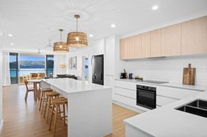 Bright modern kitchen with island, wood stools, pendant lights, and ocean view dining area