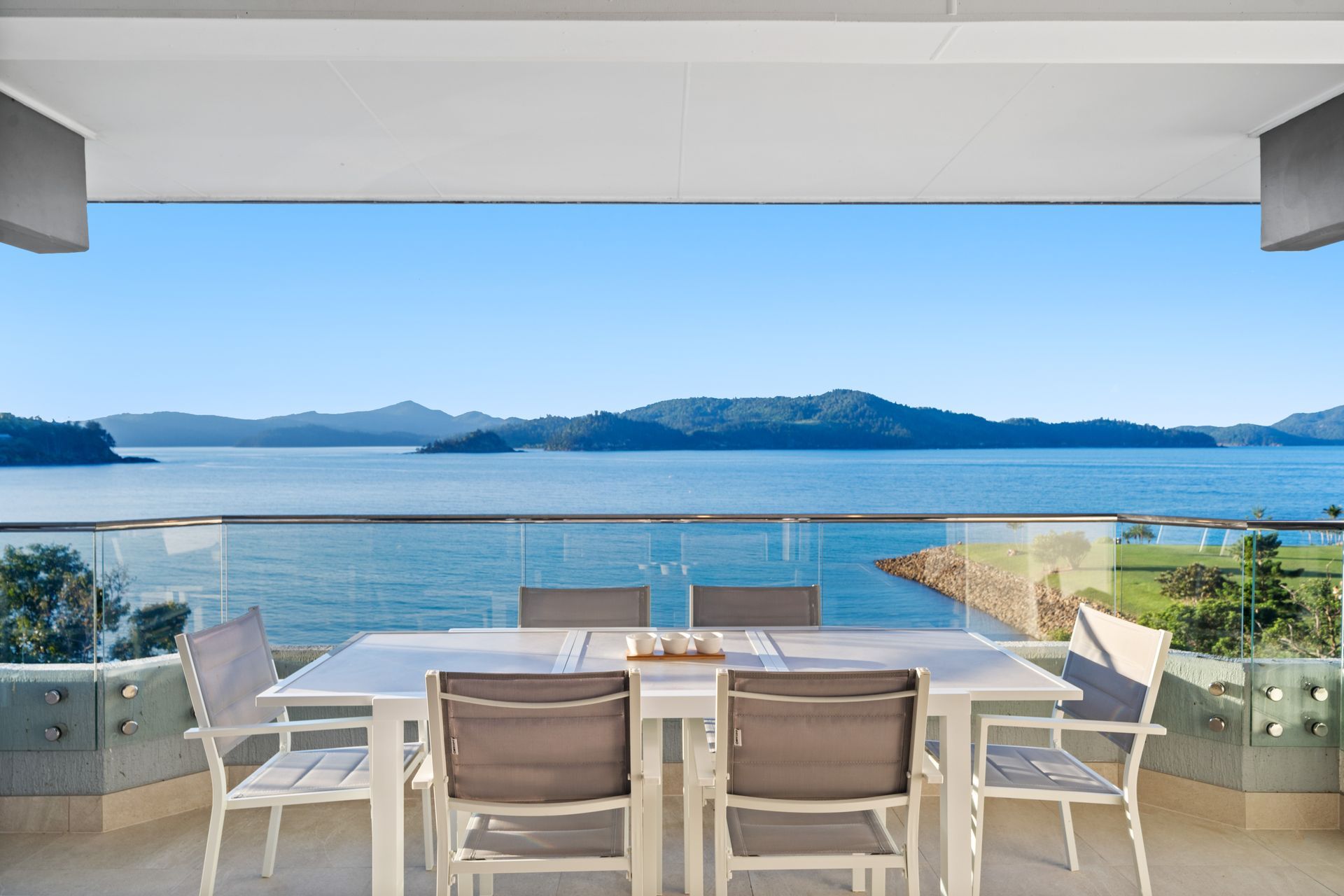 Covered balcony dining area overlooking a calm blue ocean and distant islands