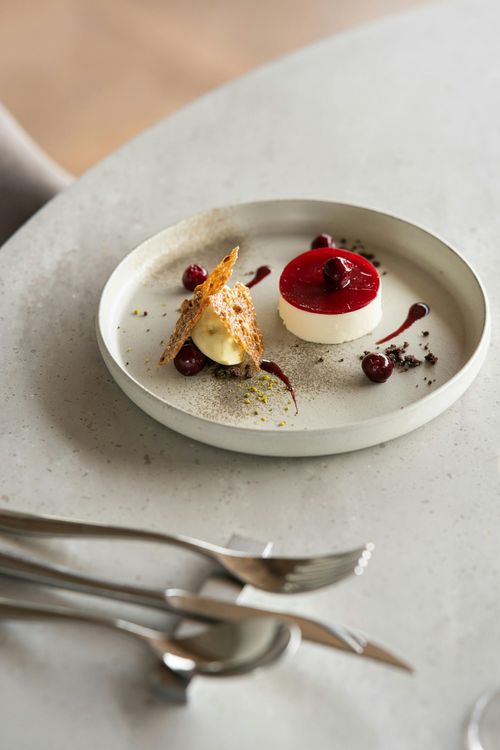 Elegant plated dessert with red berry topping and sauce on a white table, with silverware nearby