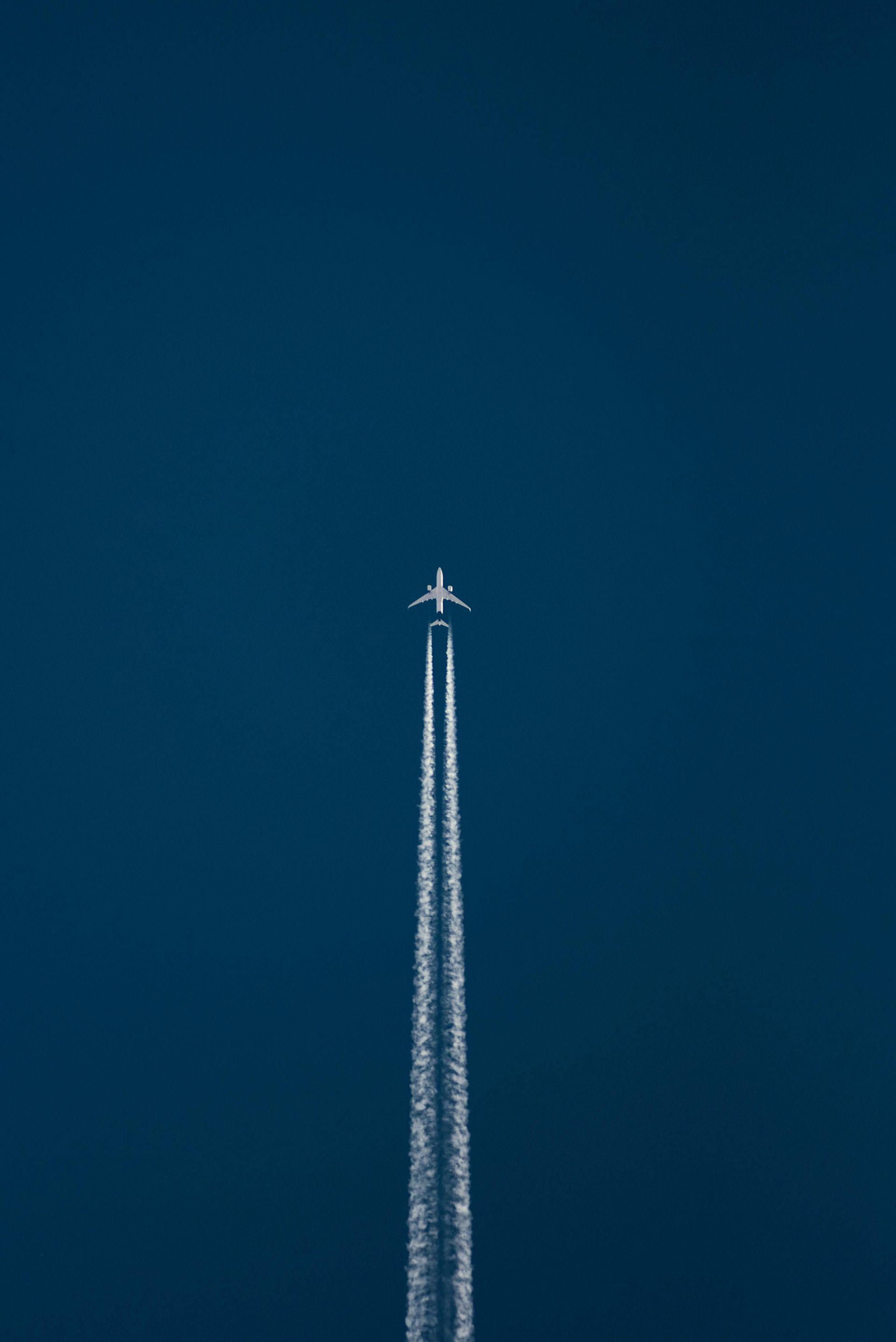 Jet aircraft leaving twin white contrails against a clear dark blue sky
