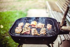 Charcoal grill with meat skewers and burgers cooking outdoors on a wooden deck