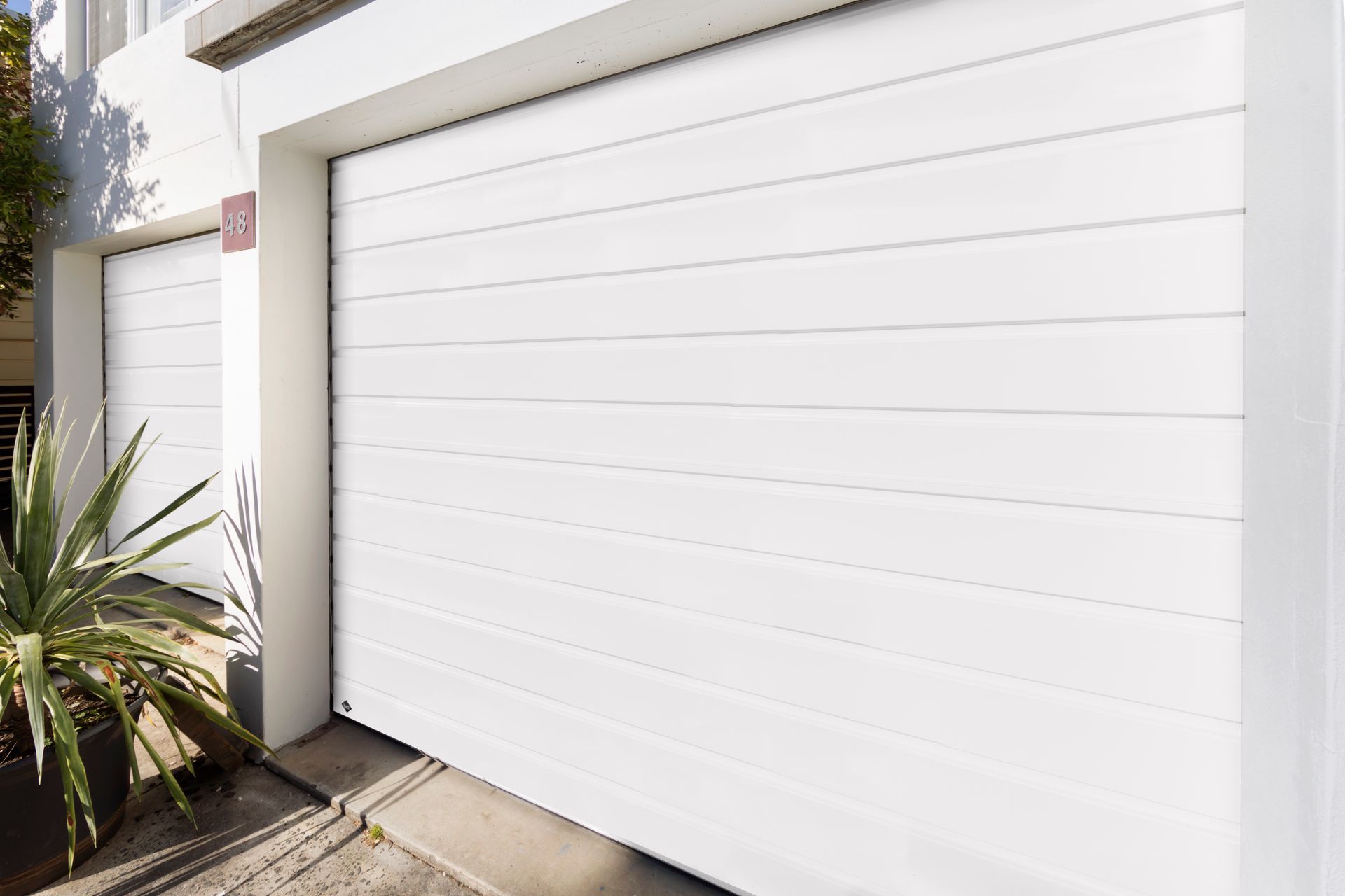 Two white garage doors are sitting next to each other on the side of a house.