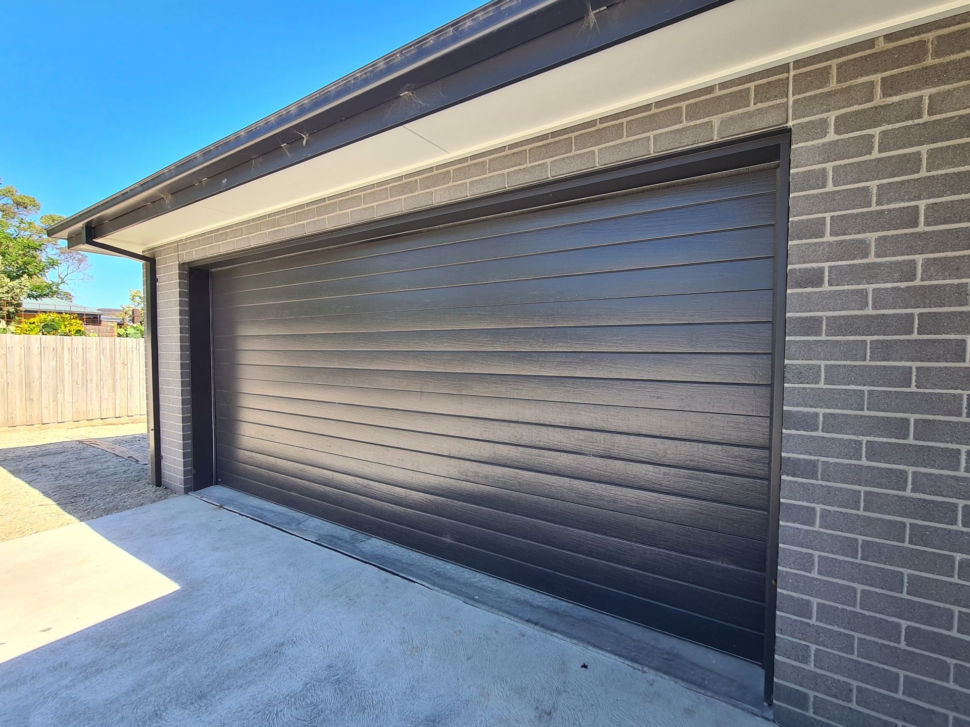 A black garage door is on the side of a brick building.