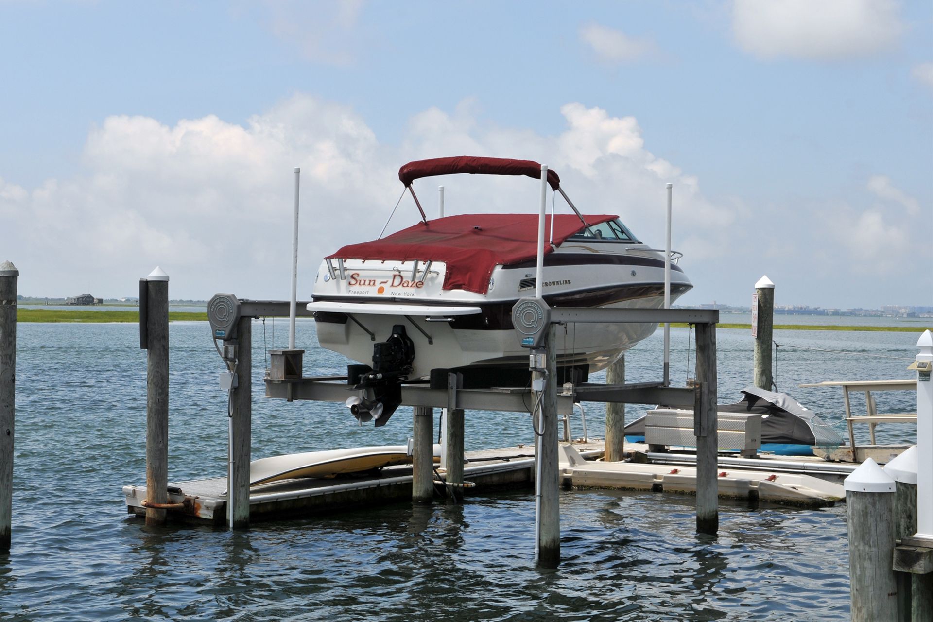 Boat on a lift in the water, covered with a red top, against a blue sky and calm ocean.