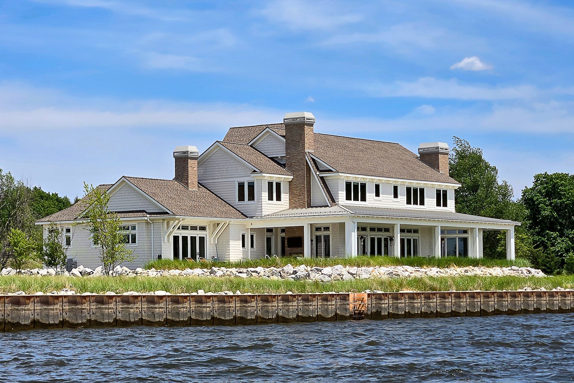 White house with tan roof and porch by the water on a sunny day.