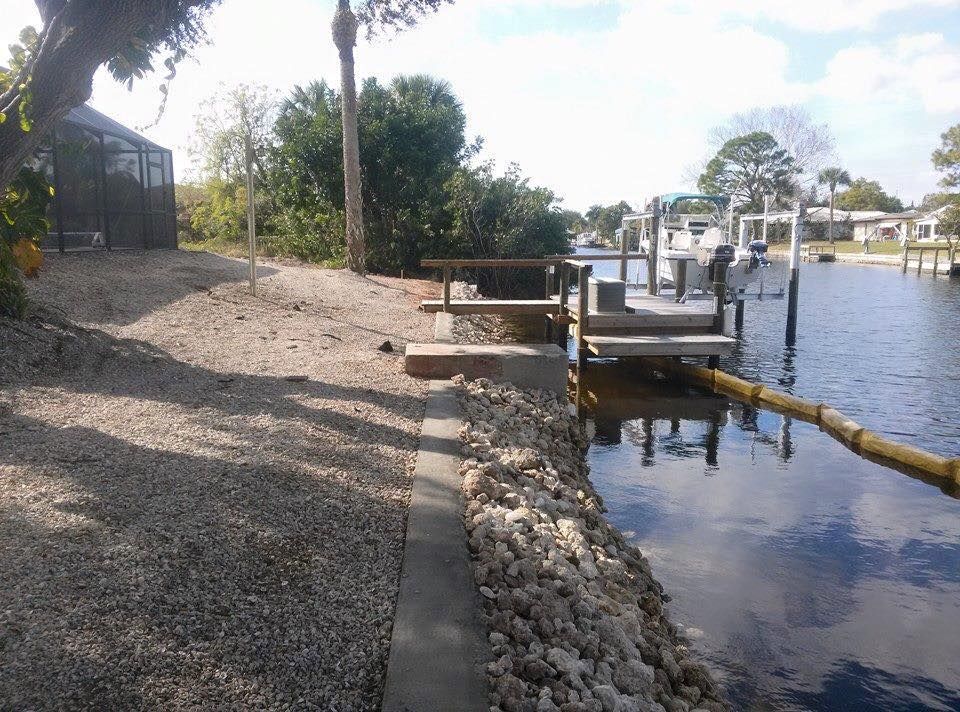 Gravel path alongside a waterway with a wooden dock and steps. Sun is shining.
