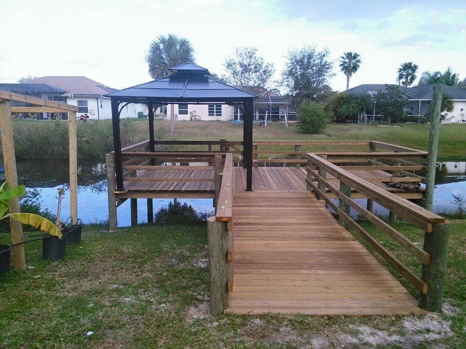 Wooden dock with gazebo over water. Bridge with railings leads to the gazebo.