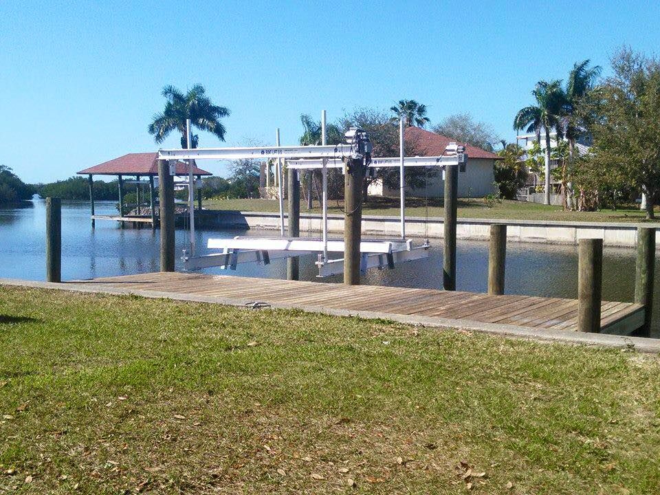 Boat lift on a canal with a dock and houses in the background on a sunny day.