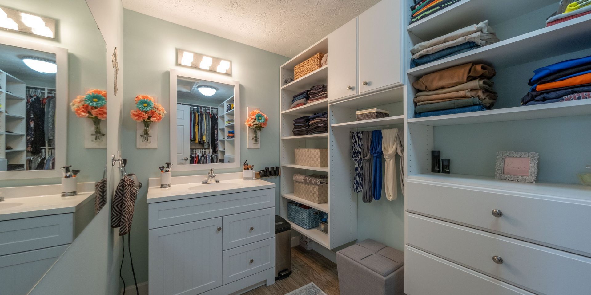 A bathroom with a sink , dresser , mirror and walk in closet.