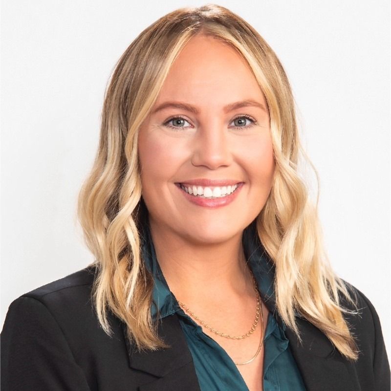 Smiling blonde woman in a black blazer and teal top against a white background