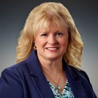 Portrait of a smiling woman with blonde hair in a blue blazer against a dark background