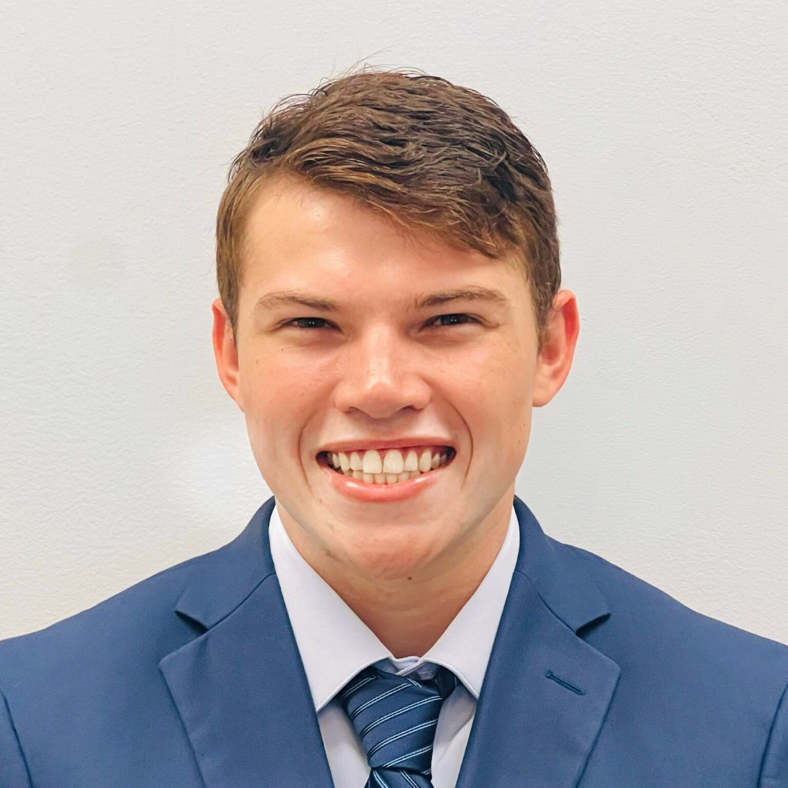 Smiling man in a blue suit and striped tie against a plain light background