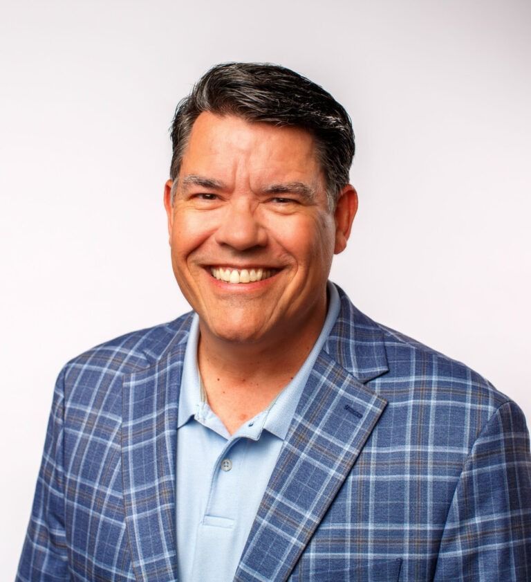 Smiling man in a blue plaid blazer and light blue shirt against a white background