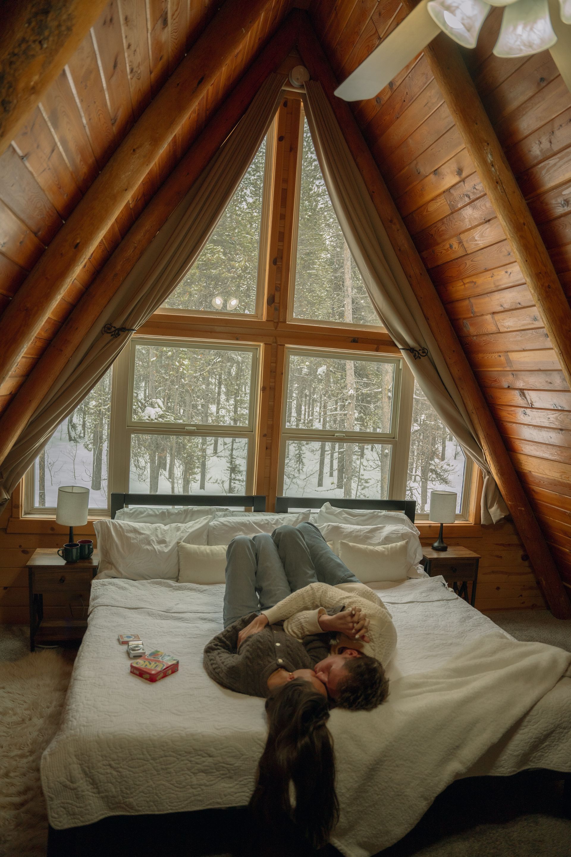 A man and woman are laying on a bed in a cabin.