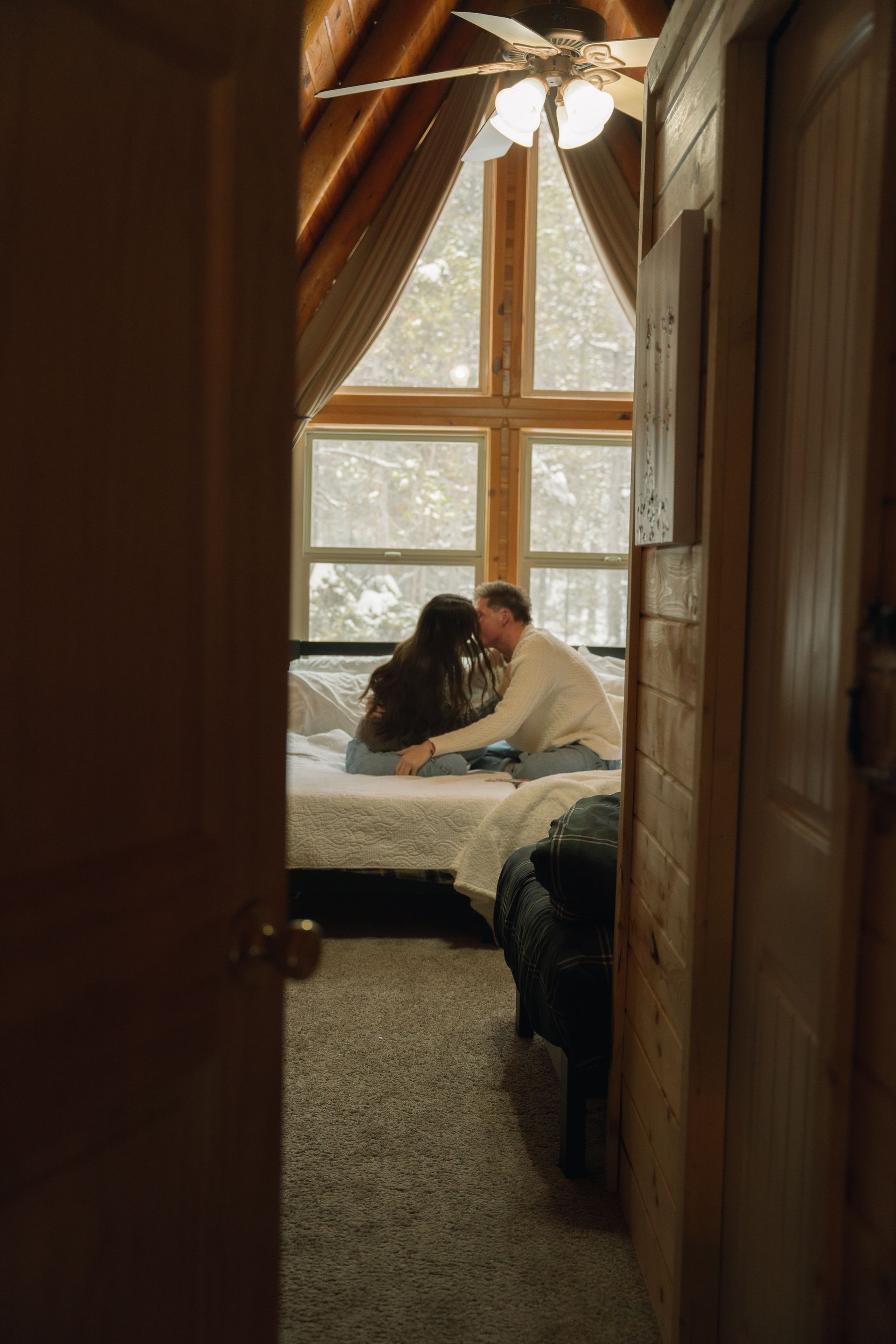 A man and a woman are sitting on a bed in a cabin.