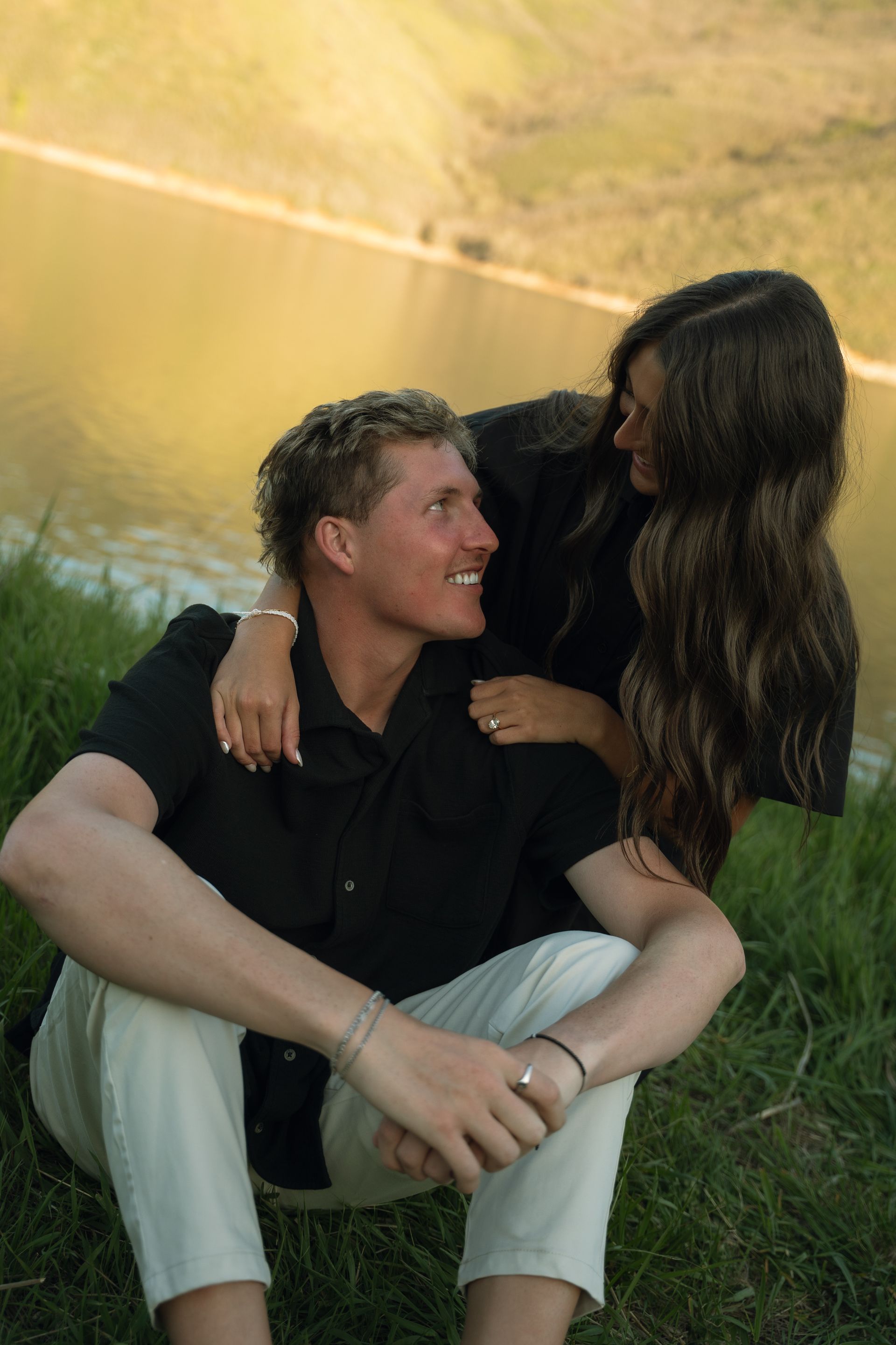 A man and a woman are sitting in the grass near a lake.