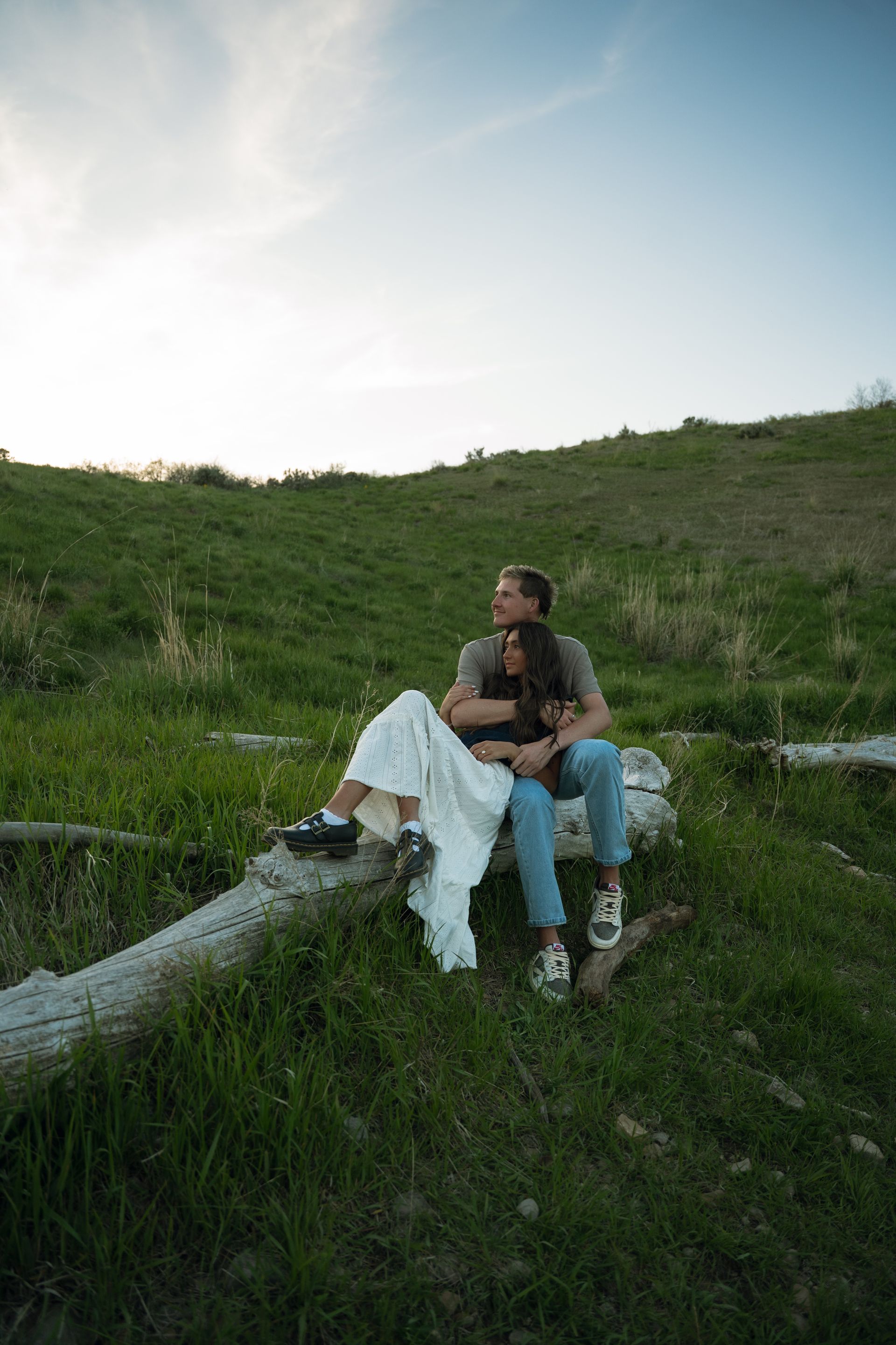 A man and a woman are sitting on a log in the grass.