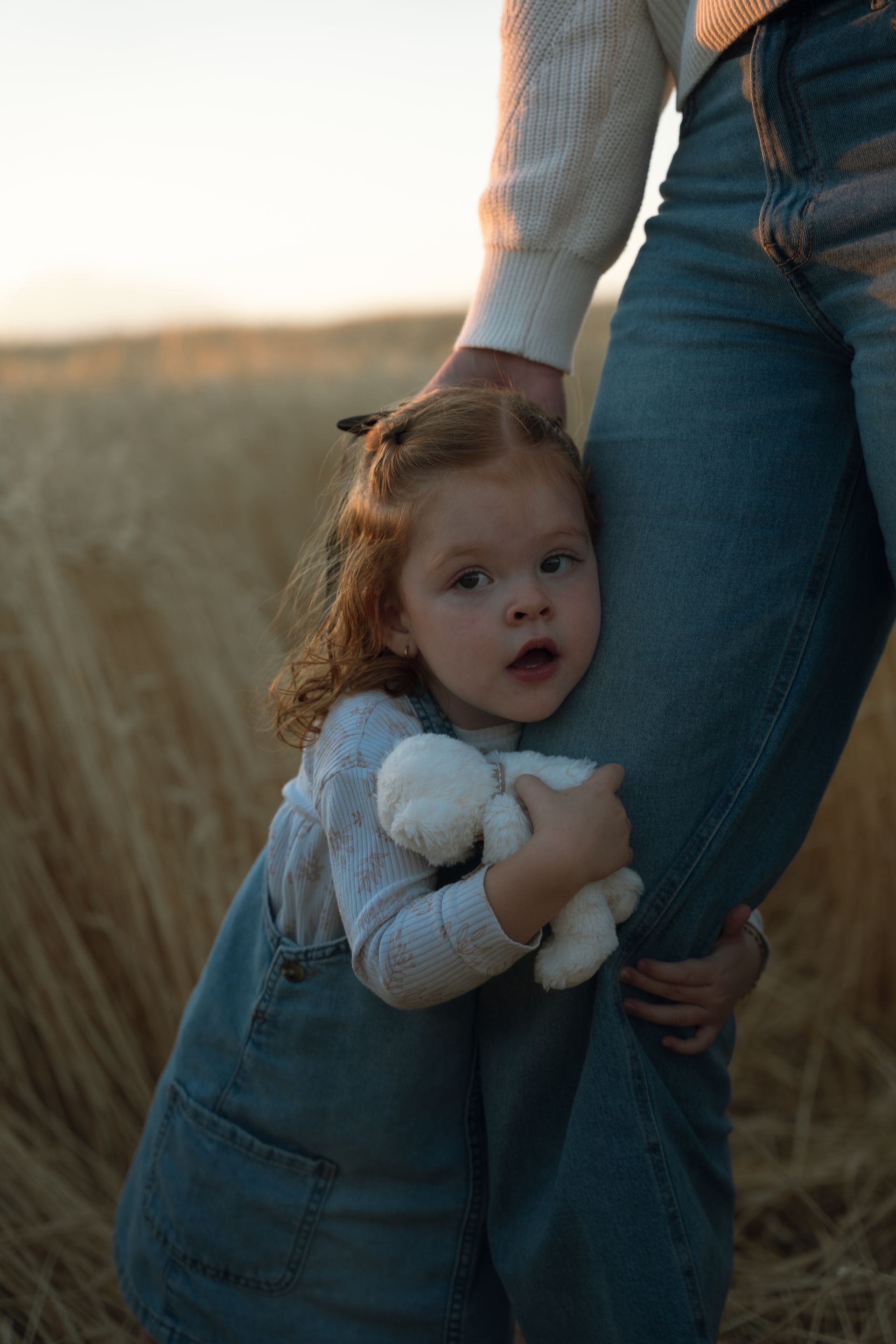 A little girl is hugging her mother in a field while holding a teddy bear.