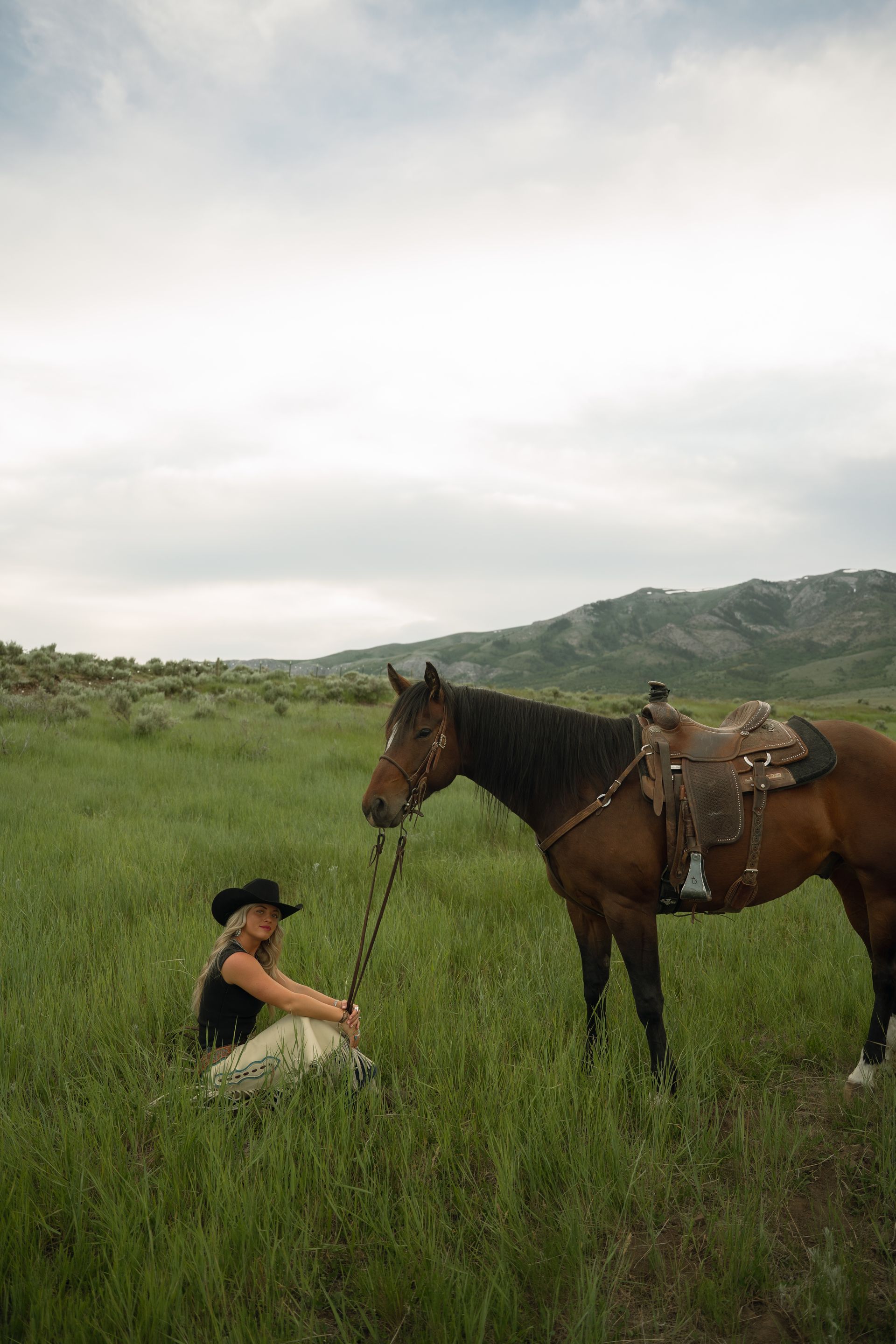 A woman is sitting next to a horse in a field.