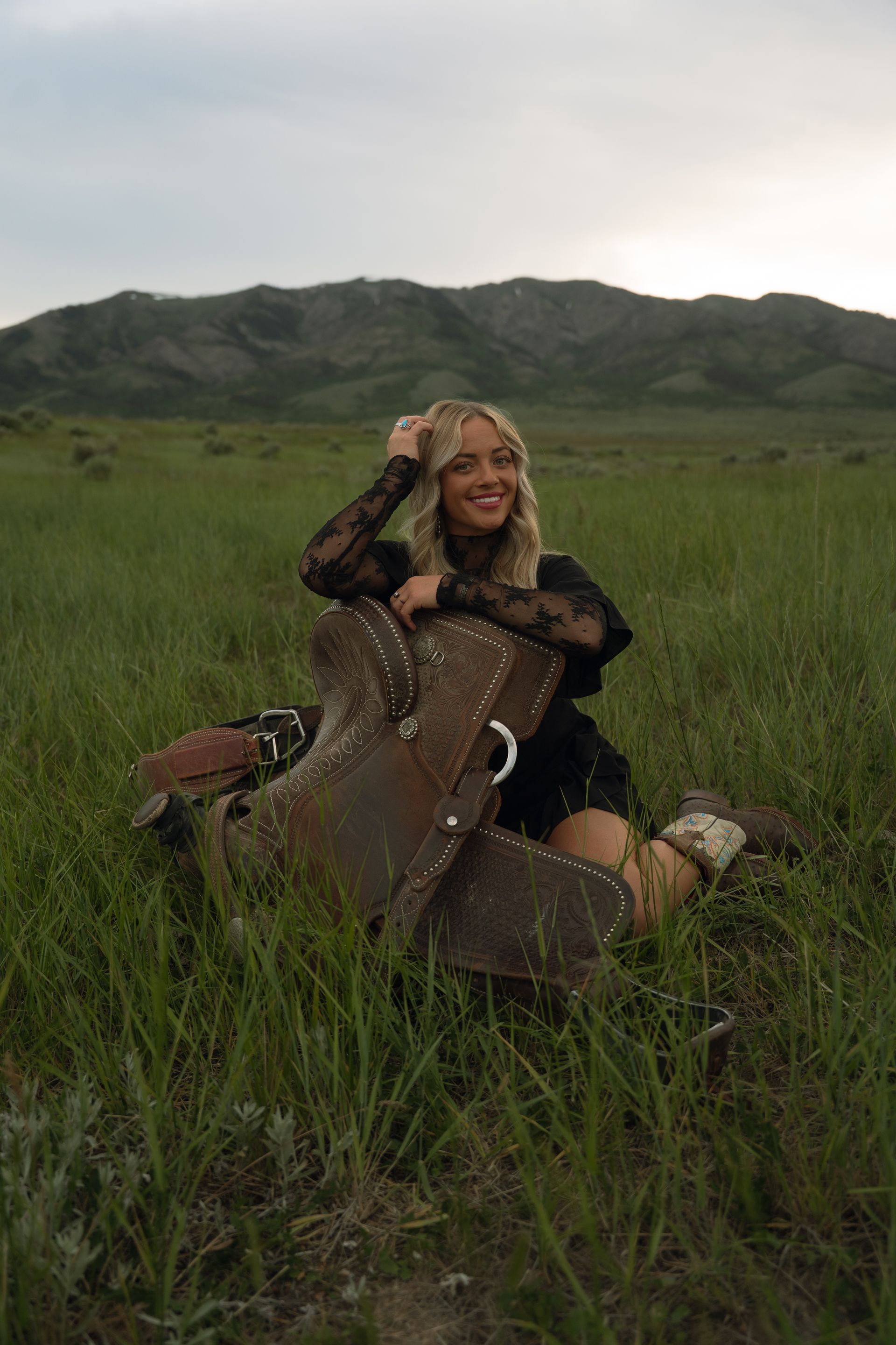 A woman is sitting in a field holding a guitar case.