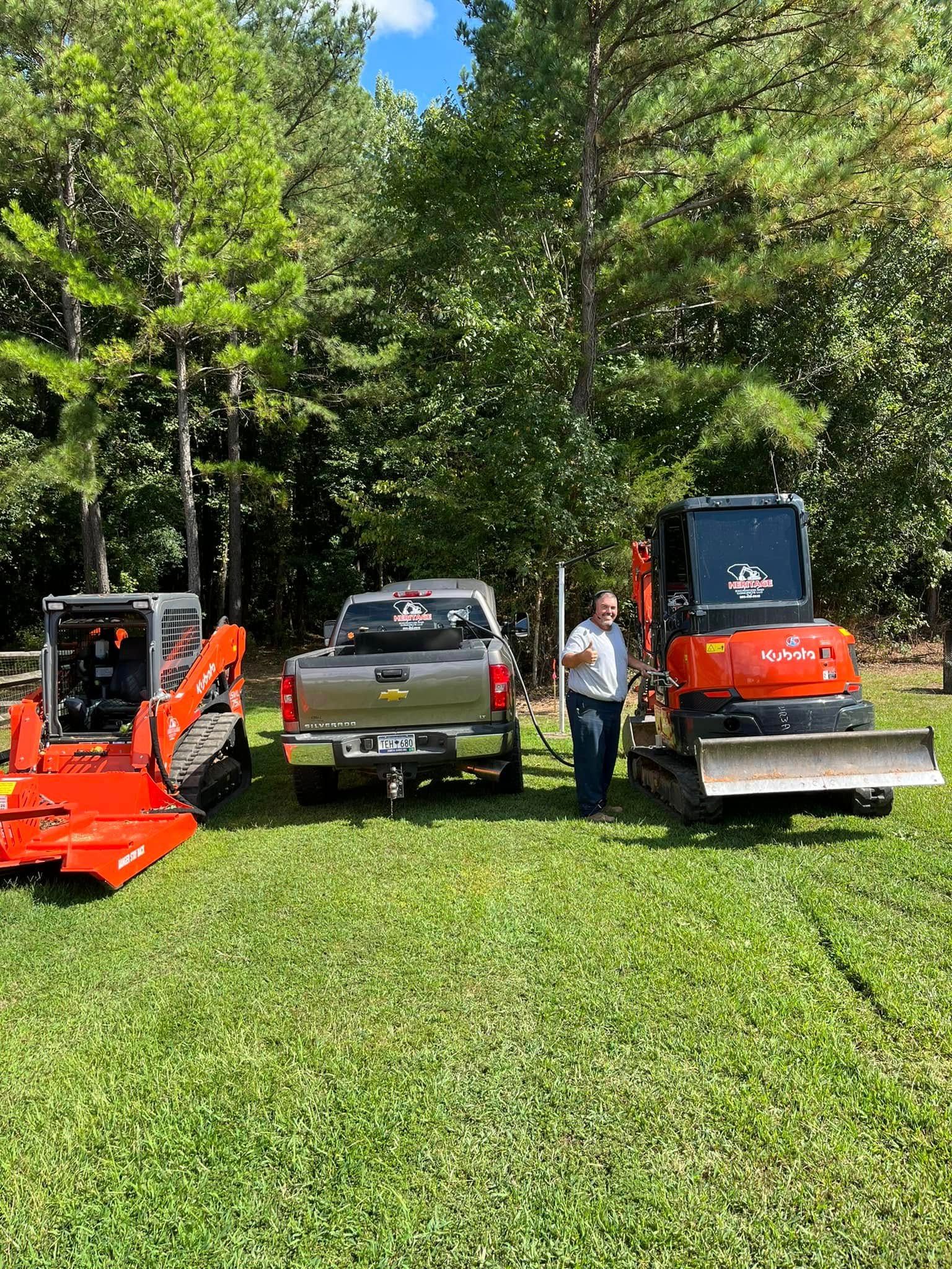 Three lawn mowers and a pickup truck on grass, with a person standing between them in a wooded area.