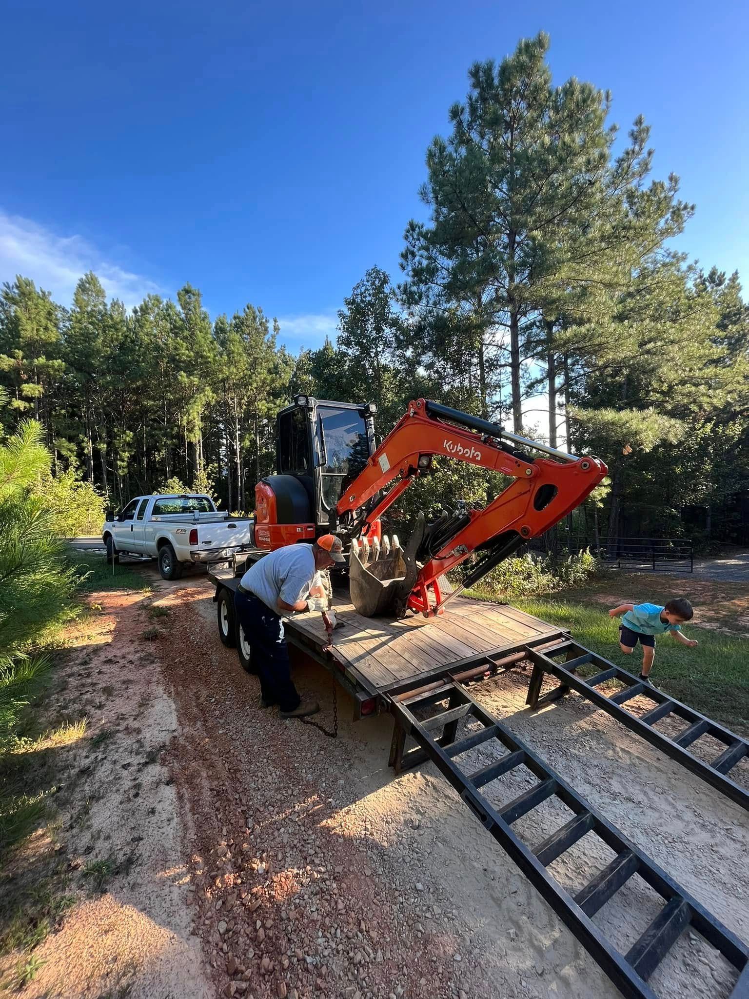 Orange mini excavator working on a dirt path beside a metal ramp in a wooded area