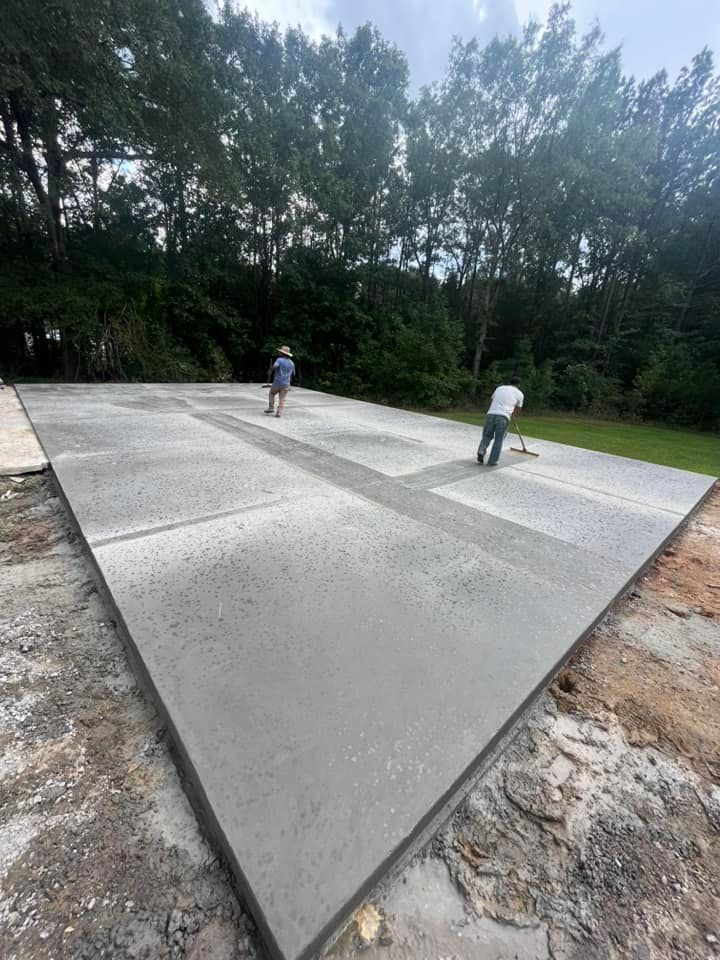 Fresh concrete slab under construction with two workers smoothing the surface near a tree line