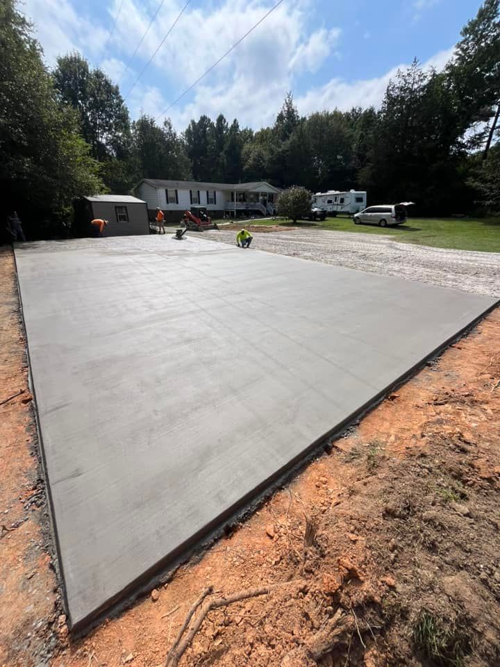 Freshly poured concrete slab at a construction site with workers and vehicles in the background