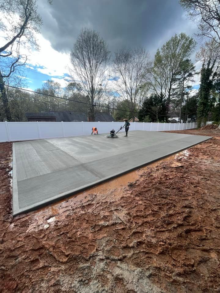 Outdoor ice rink under construction with workers on a gray day, surrounded by trees and muddy ground