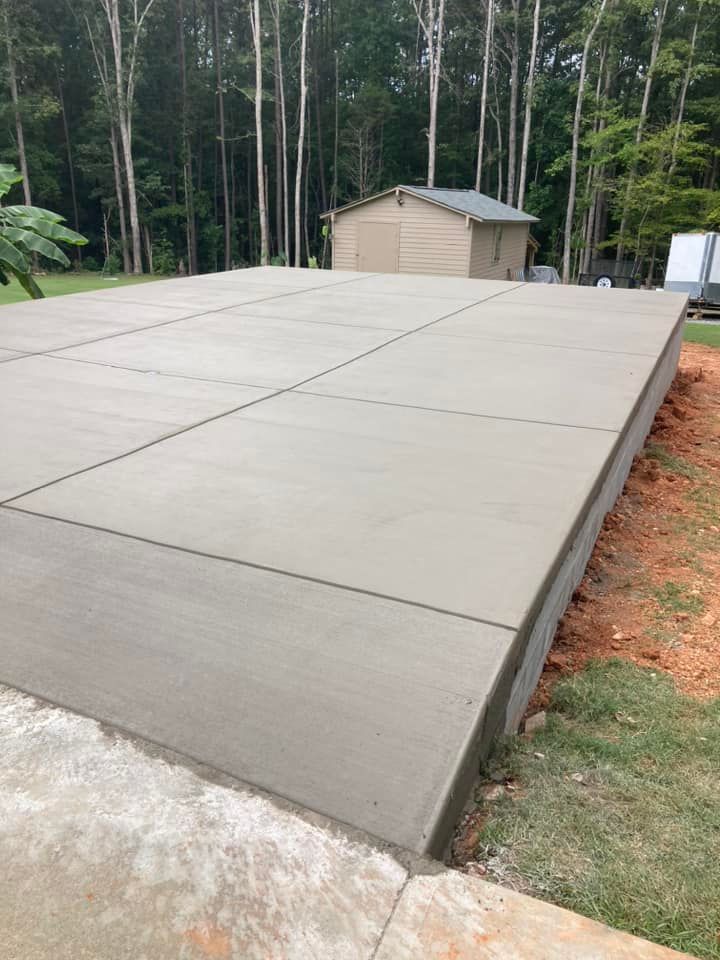 Fresh concrete slab foundation in a wooded yard near a small beige shed