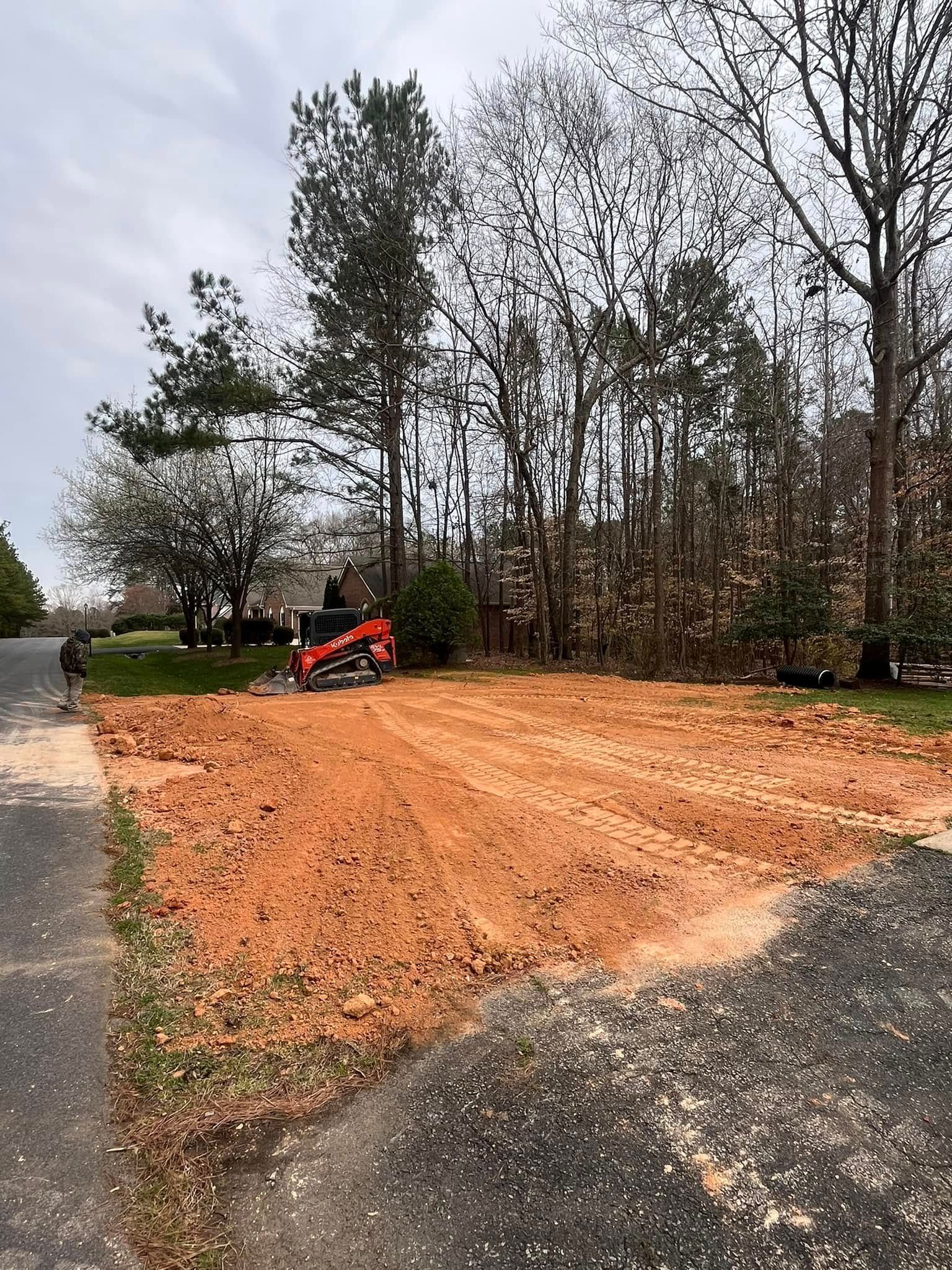 Orange wood chips spread beside a road, with a red skid-steer loader and trees in the background