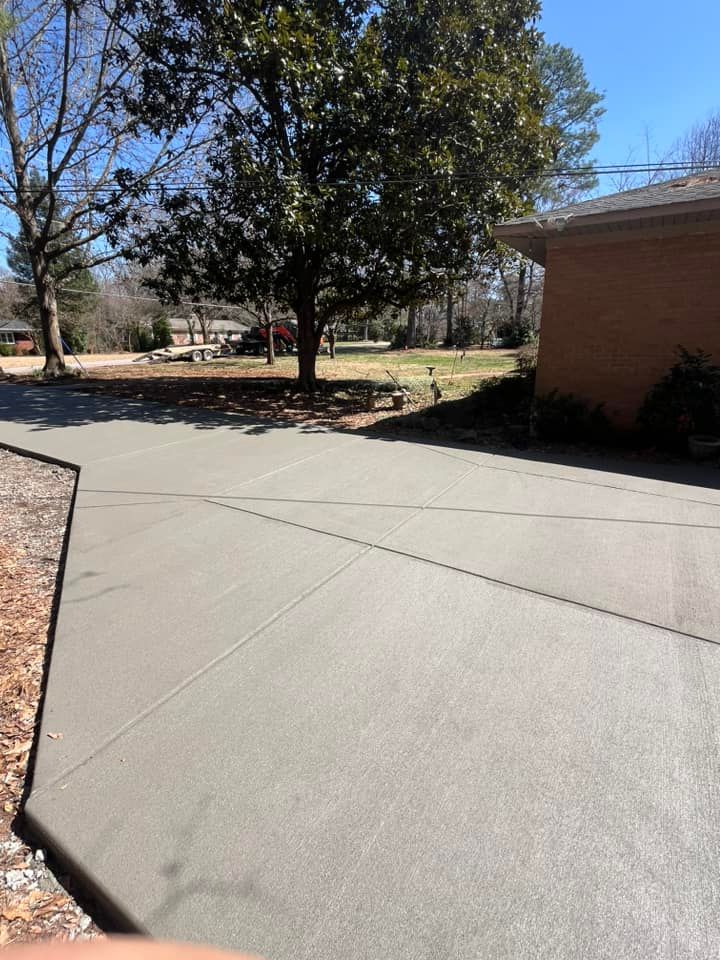 Concrete walkway beside a brick building, with trees and dry landscaping in bright sunlight.