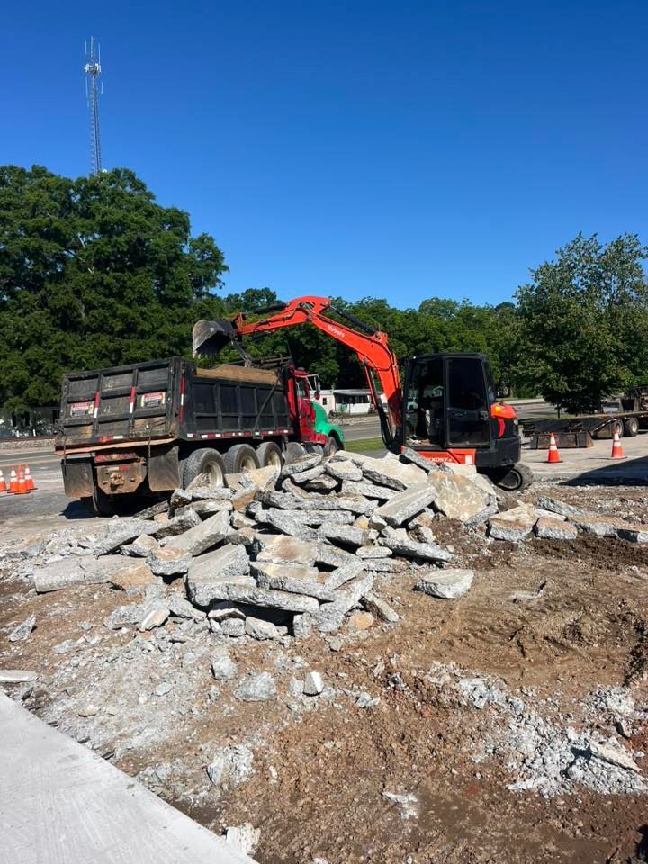 Construction site with excavator and dump truck beside a pile of broken concrete rubble