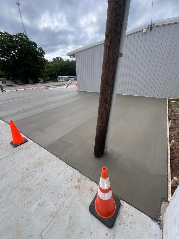 Outdoor work area with orange cones, a wooden pole, and a concrete ramp beside a metal building.