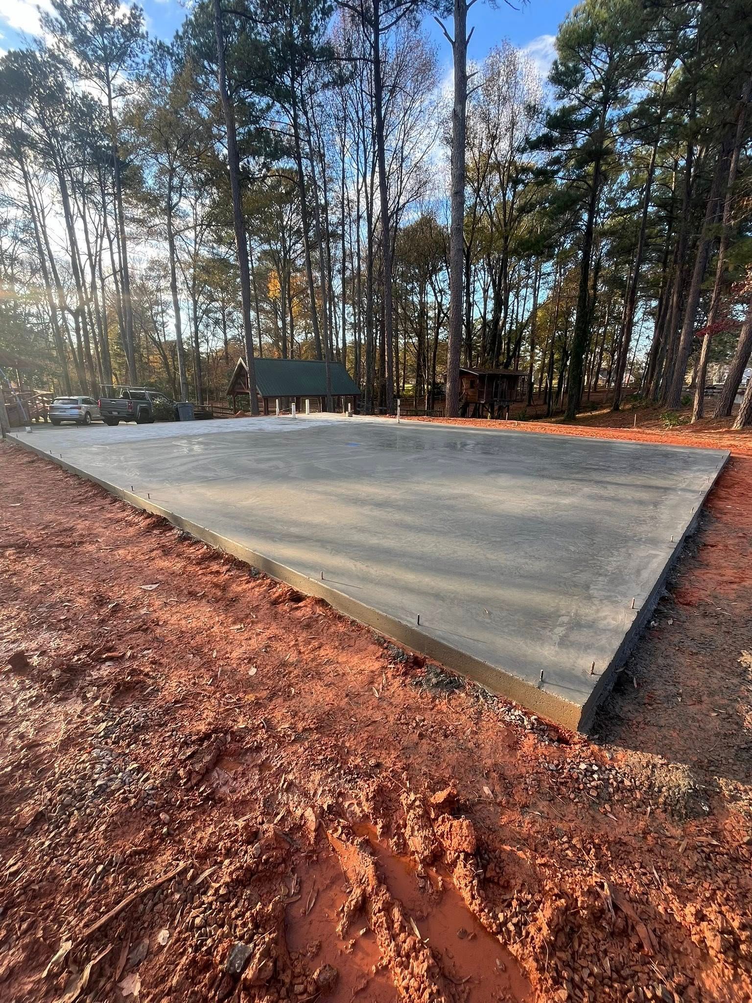 Concrete slab in a wooded clearing with red dirt foreground and tall trees in the background