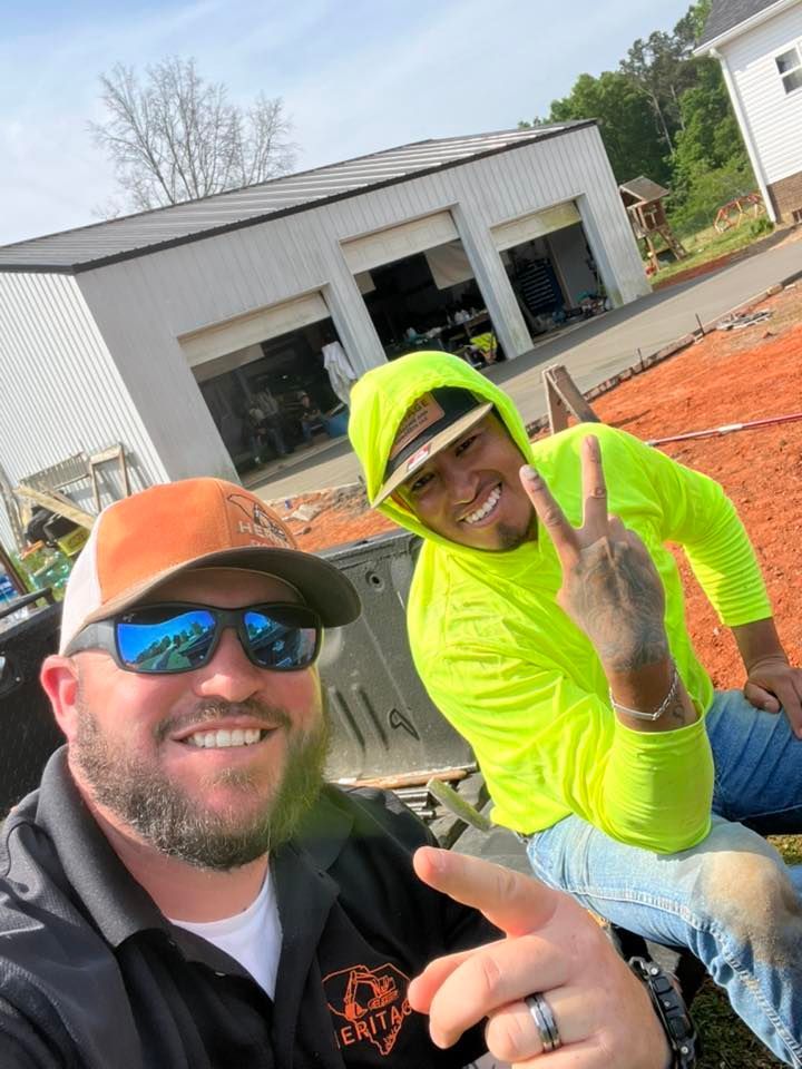 Two workers in neon safety shirts and hard hats smiling outdoors at a construction site, giving peace signs