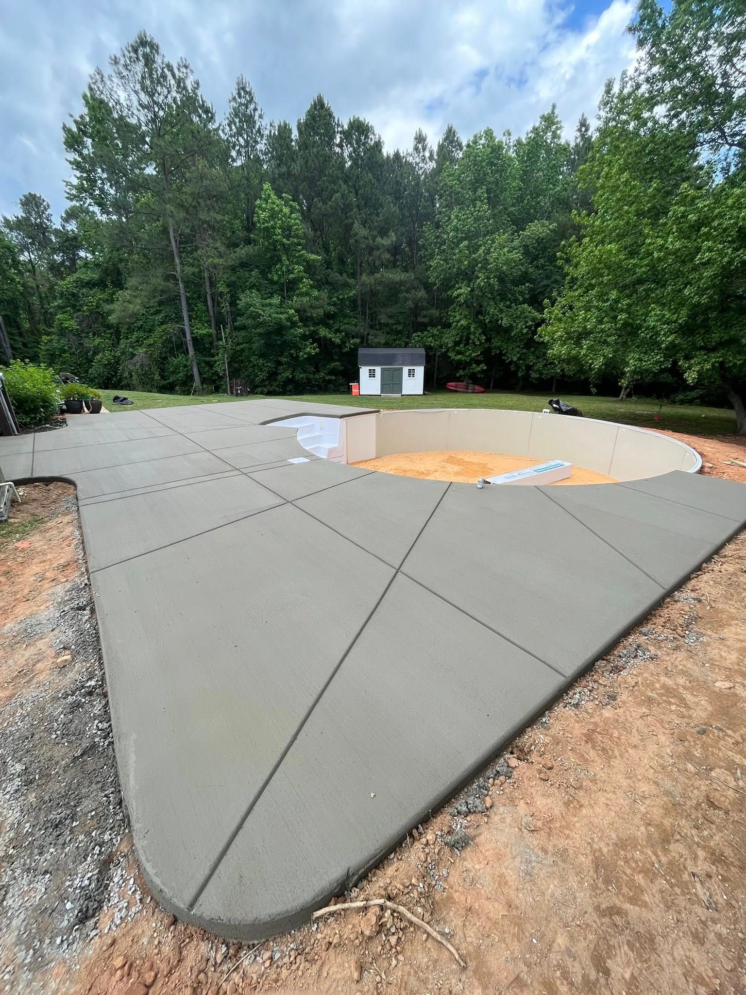 Concrete patio under construction with curved edge, orange tarp, and trees in the background