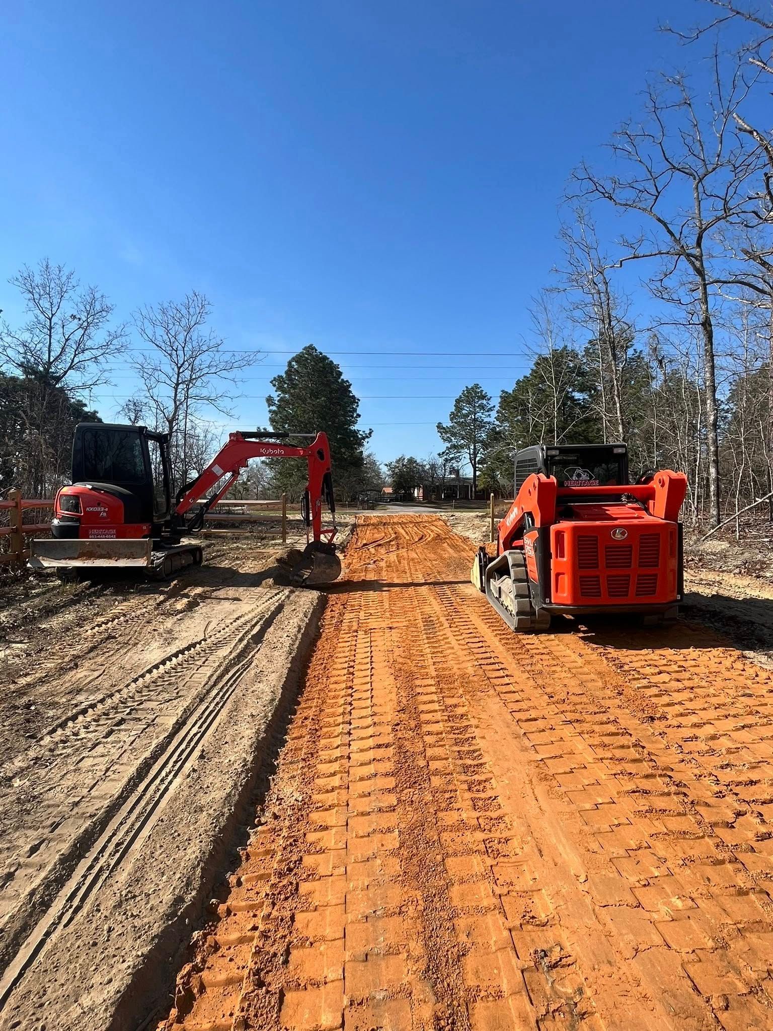 Construction site with red excavators clearing a dirt road under a blue sky