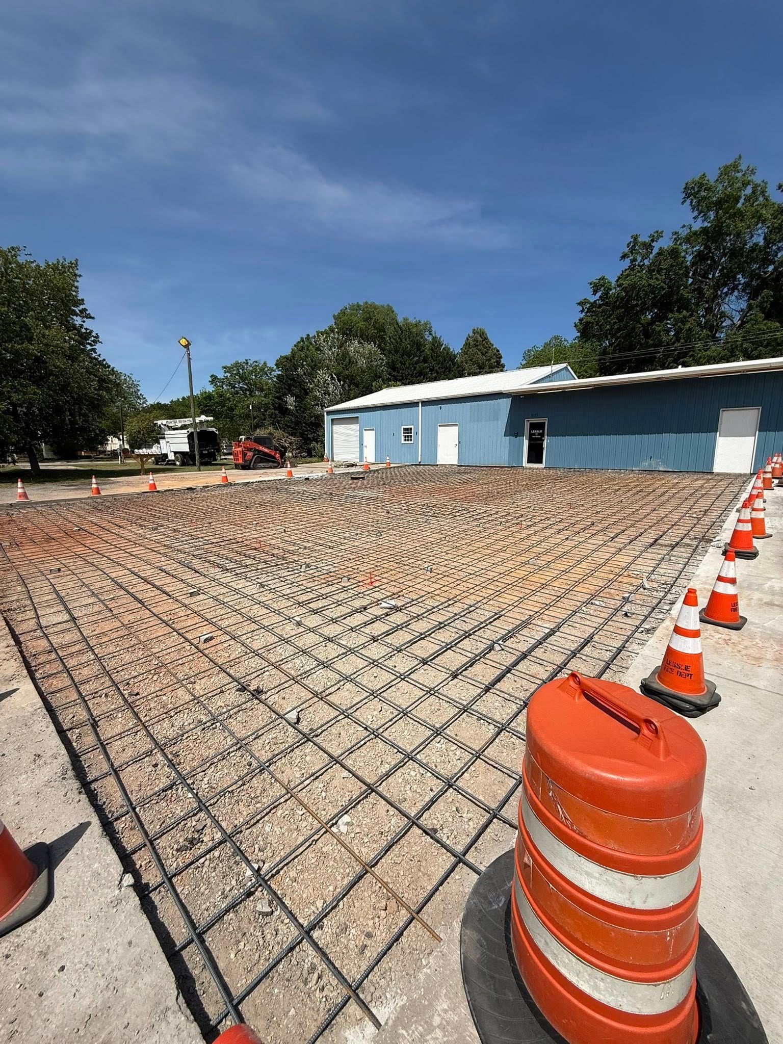 Chain-link fence over gravel lot with orange construction cones beside a blue building under a clear sky