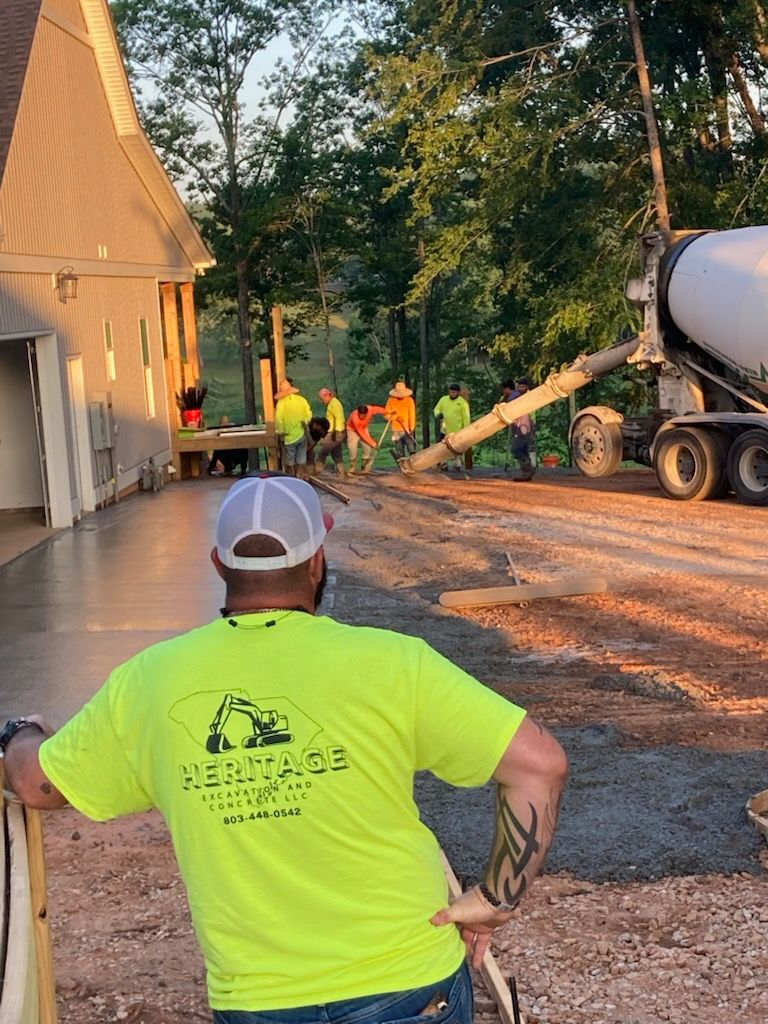 Workers in neon shirts near a cement truck pouring gravel beside a house at dusk