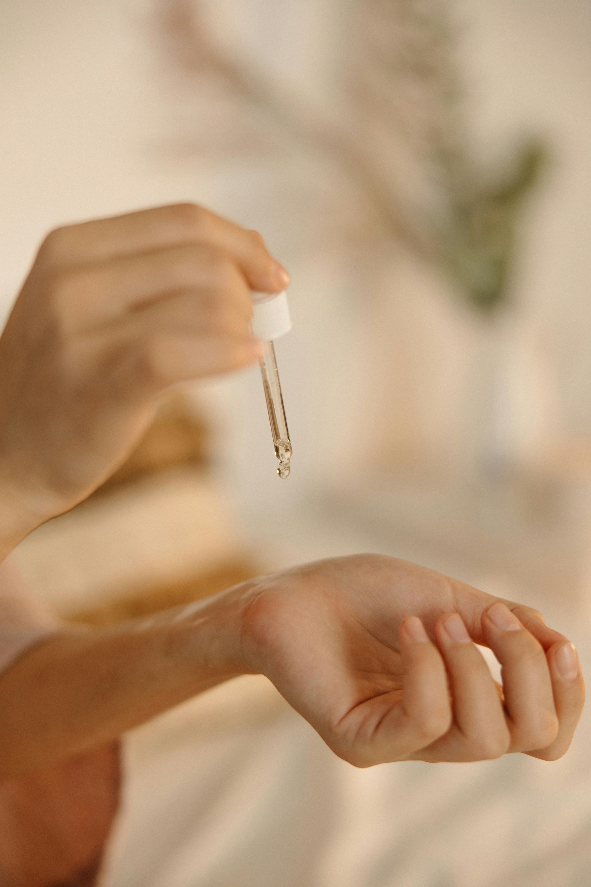 Person using a dropper to apply liquid to their wrist; neutral background.