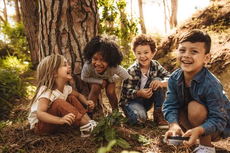 A group of children are sitting under a tree in the woods.