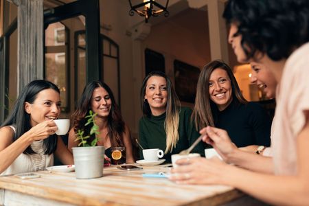 A group of women are sitting at a table drinking coffee.