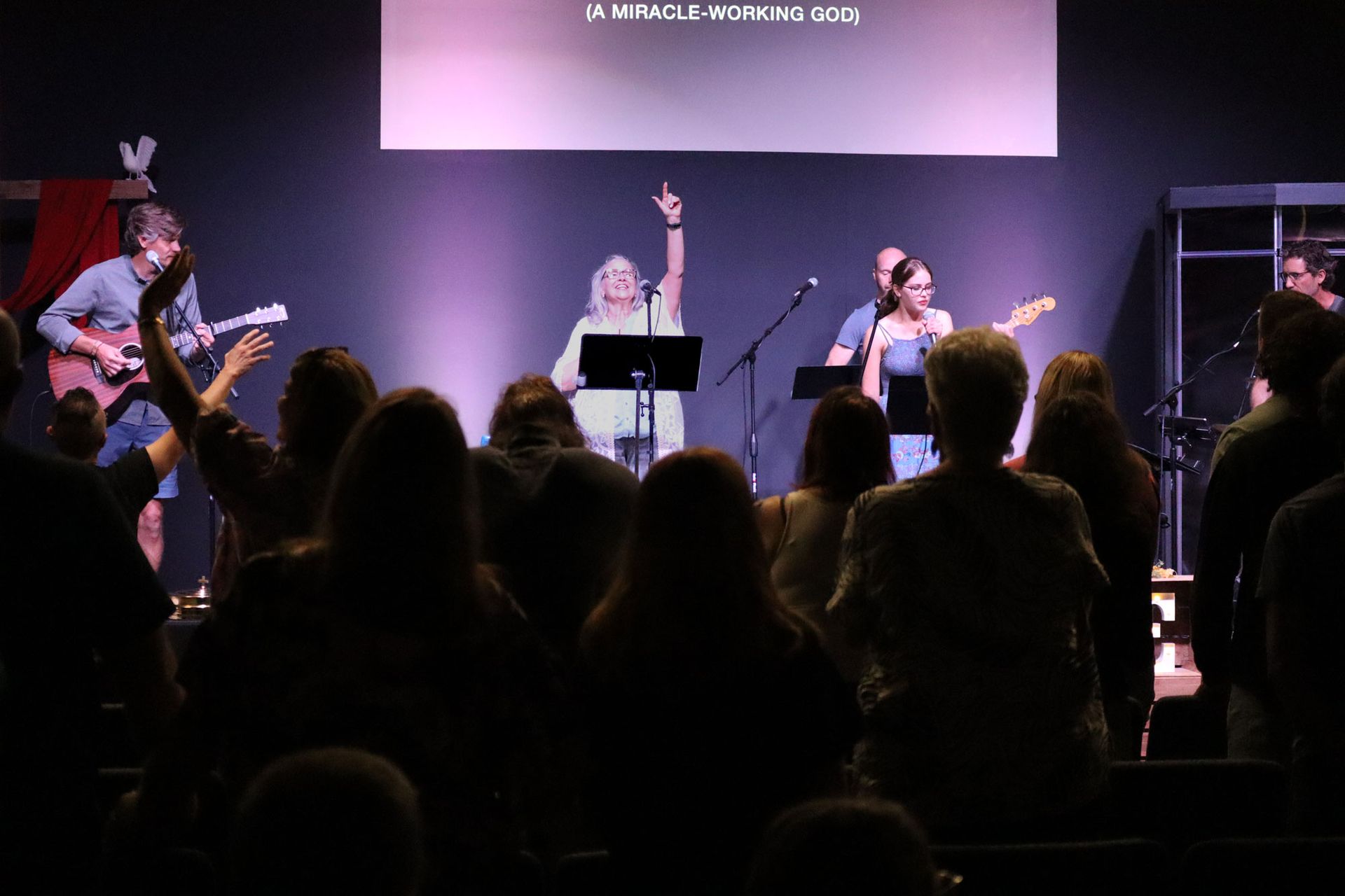 A group of people are standing in front of a stage in a dark room.
