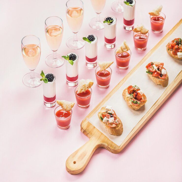 Pink-toned spread with champagne, layered shots, and bruschetta on a wooden board.