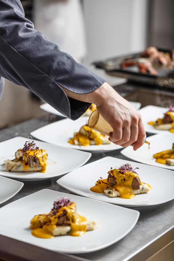 Chef plating gourmet dishes on white plates in a kitchen.